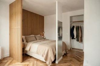 Suite parentale de 15m2 avec cloison basse en bois naturel séparant le coin lit du dressing dans un appartement moderne