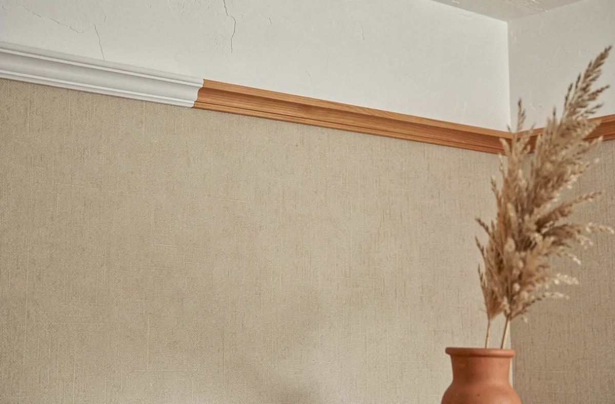 Détail de papier peint beige mat en chambre avec corniche blanche et herbe de pampa en pot terracotta