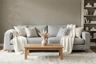Salon gris et blanc cosy avec canapé en lin gris clair, coussins ivoire et plaid blanc en maille, ambiance chaleureuse et moderne